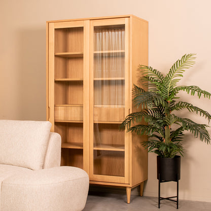 Vitrinekast Jule naturel eikenhout, schuin vooraanzicht in een interieur